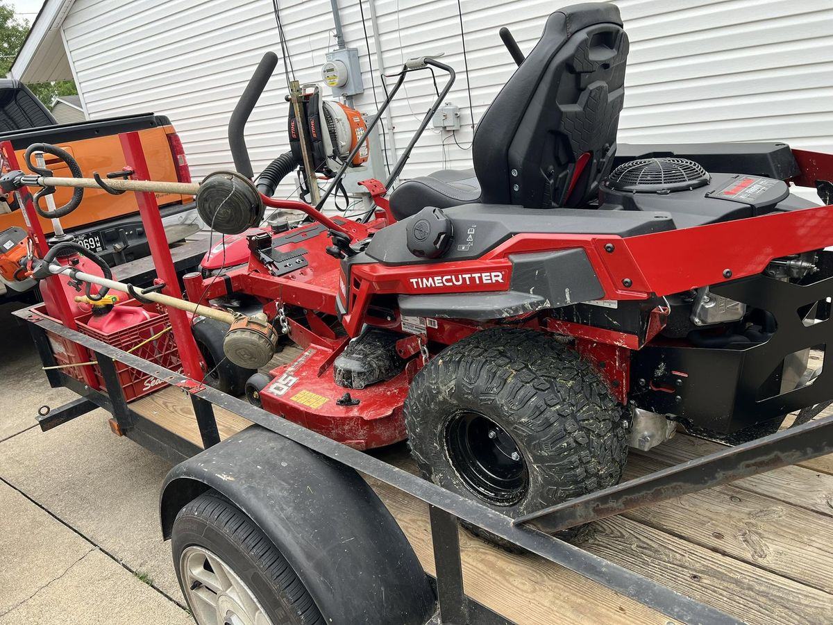 The red Toro TimeCutter strapped on the open trailer, Stihl trimmers racked beside it